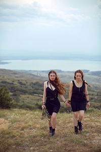 Two woman in black dresses walk on the mountain with a bouquet of flowers in summer at sunset