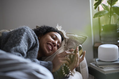 Smiling young woman lying on sofa and using phone