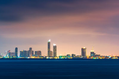 Sea by illuminated buildings against sky in city