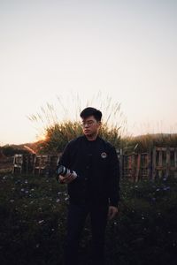 Portrait of young man standing on field against clear sky