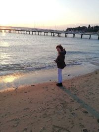 Full length of boy standing on beach against sky during sunset