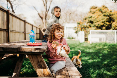 Brother and sister eating sandwich and smiling in backyard