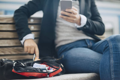 Midsection of woman using mobile phone by open bag while sitting on bench