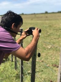 Man photographing while standing by fence on field