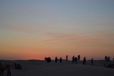Silhouette people on sand dune in desert against sky during sunset