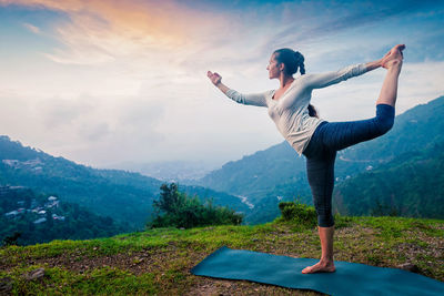 Woman doing yoga asana natarajasana outdoors at waterfall
