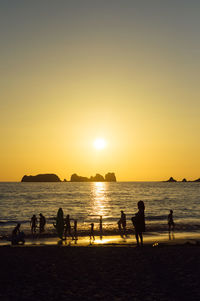 Silhouette people at beach against sky during sunset