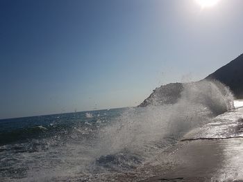 Sea waves splashing on shore against clear sky