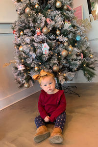 Baby girl sitting against christmas tree