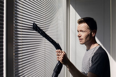 Man cleaning dust from window blind by vacuum cleaner at home. themes housework and housekeeping.