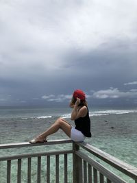 Woman sitting by sea against sky