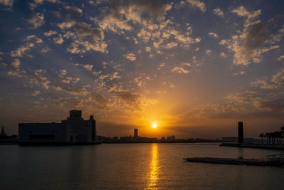 Buildings by sea against sky during sunset