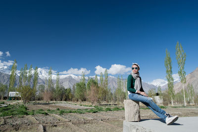 Full length of young man sitting on land against sky