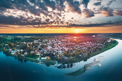 Aerial view of city by river against cloudy sky during sunset