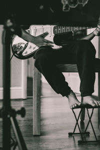 Low section of man playing guitar while sitting on chair at home