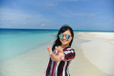 Portrait of smiling young woman standing at beach against sky