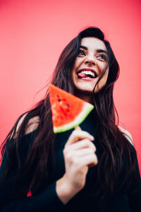 Portrait of smiling young woman eating apple against red background