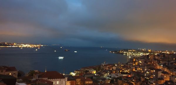 High angle view of illuminated city by sea against sky