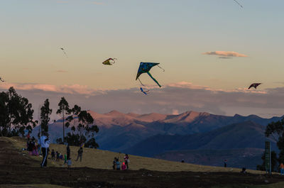 People flying kites on mountains at sunset