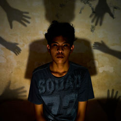 Portrait of young man standing against wall at home