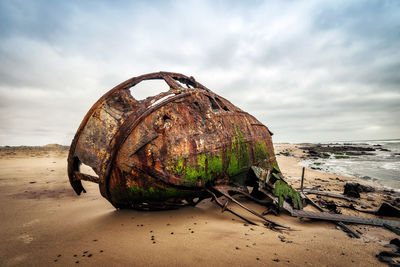 Rusty abandoned boat at beach against sky