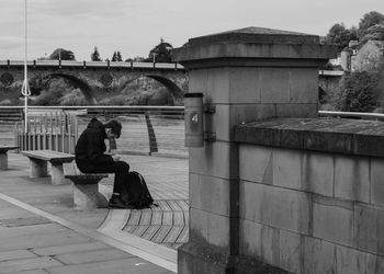 Side view of man sitting on bridge over water