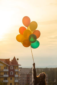 Woman holding multi colored balloons against sky during sunset