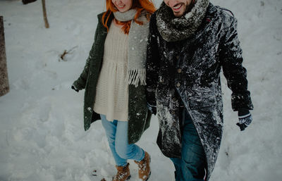 Midsection of couple holding hands walking on snow covered land in forest