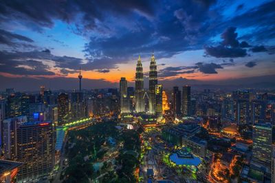 Aerial view of illuminated cityscape against cloudy sky at dusk