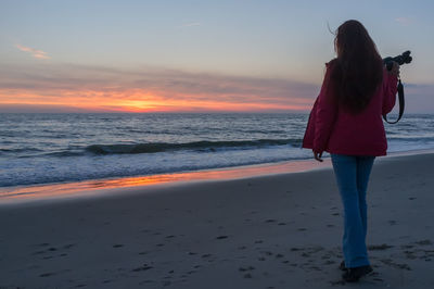 Rear view of woman standing on beach during sunset