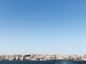 Buildings by sea against clear blue sky