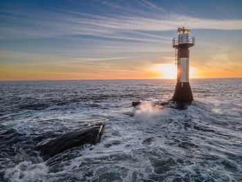 Lighthouse by sea against sky during sunset