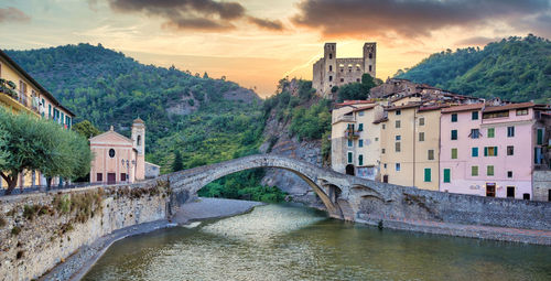 Arch bridge over river amidst buildings against sky