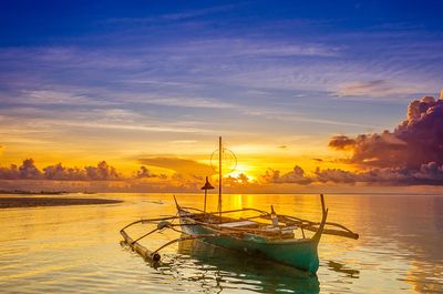 Sailboats moored in sea against sky during sunset