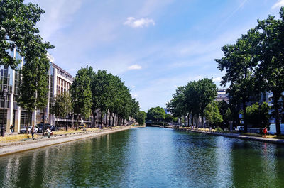 Canal amidst trees and buildings against sky