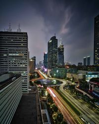 Light trails on road amidst buildings against sky at night