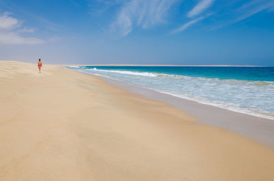 Scenic view of woman walking on empty beach against sky