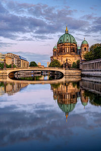 Arch bridge over river by buildings against sky