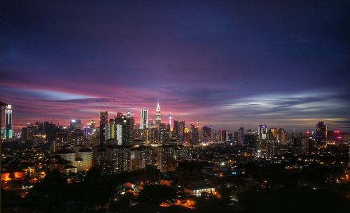 Illuminated modern buildings in city against sky at night