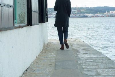Low section of woman standing on footpath by water