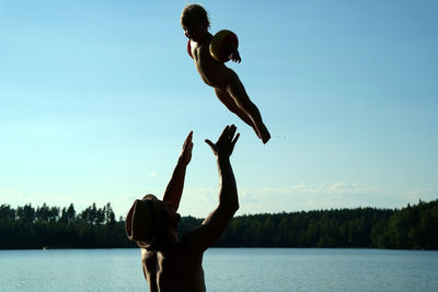 Man throwing girl while playing in lake against sky