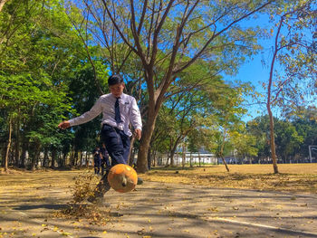 Full length of student kicking ball on street during autumn
