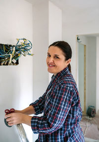 Portrait of smiling young woman standing against wall at home