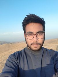 Portrait of young man wearing eyeglasses against sky