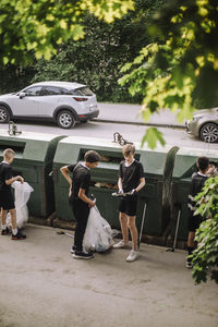 Full length of boys holding garbage bag with plastic by recycling bin