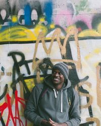 Portrait of young man standing against graffiti wall