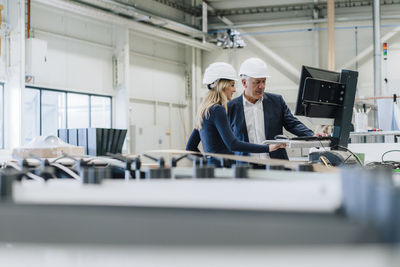 Businessman and colleague working on desktop pc in factory