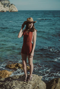 Woman wearing hat standing on rock against sea
