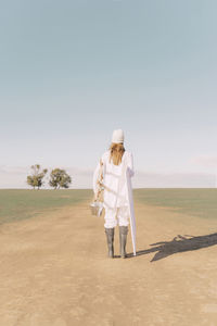 Young woman carrying easel and empty canvas on dry field