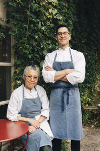 Portrait of confident male chef standing by senior female colleague outside restaurant